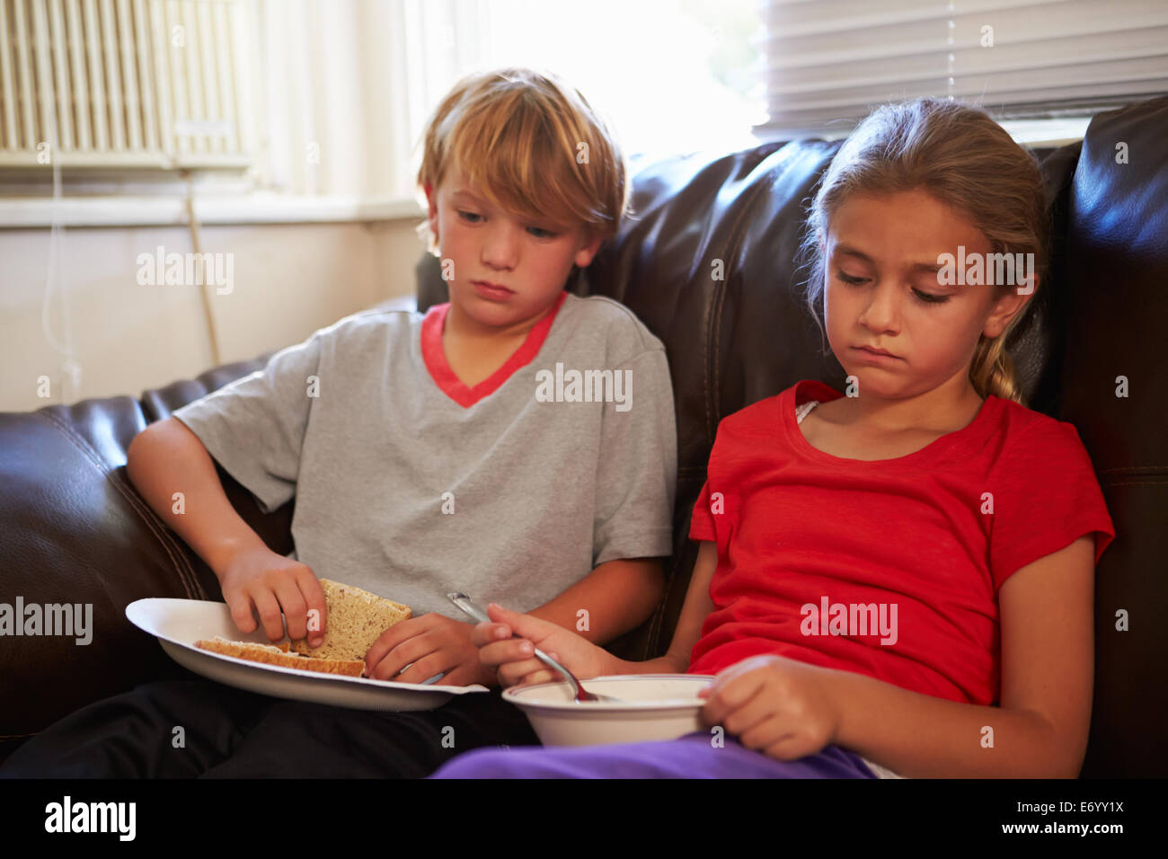 I bambini con dieta povera di mangiare pasto sul divano di casa Foto Stock