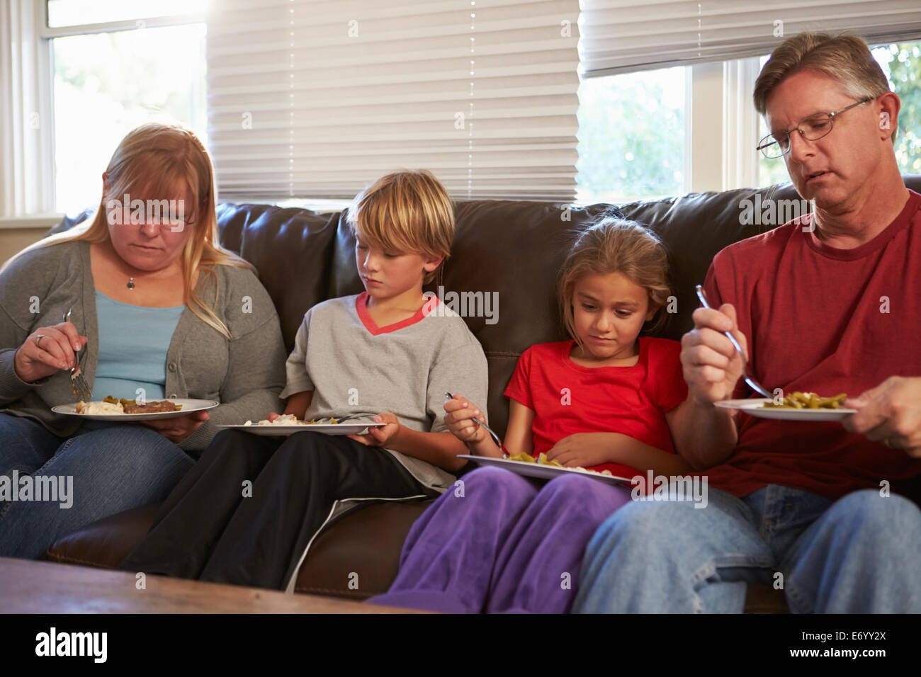 Famiglia con dieta povera di seduta sul divano a mangiare pasti Foto Stock