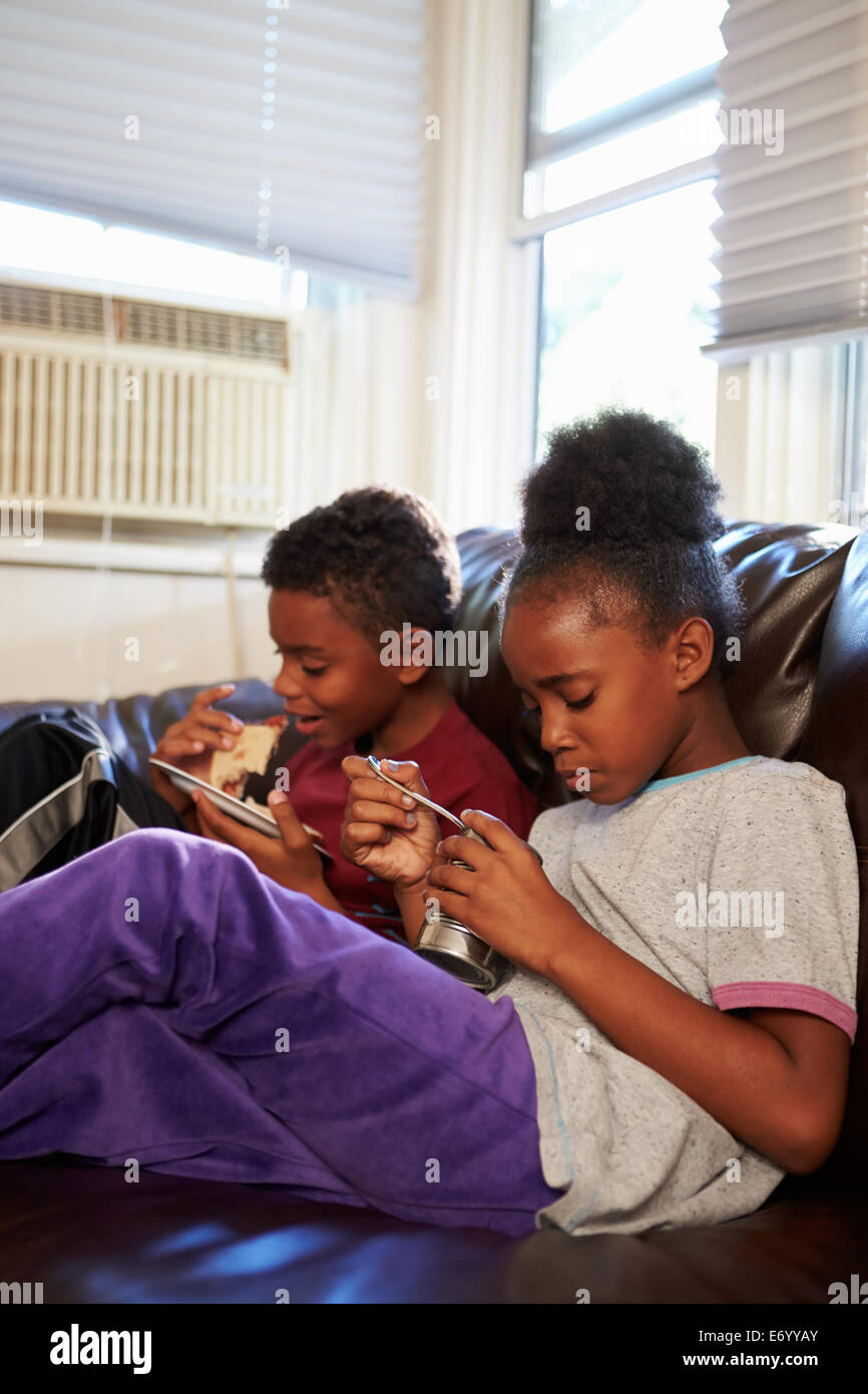I bambini con dieta povera di mangiare pasto sul divano di casa Foto Stock