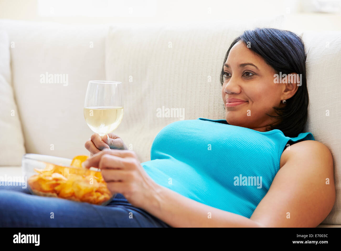 Donna sovrappeso a casa a mangiare patatine e bere il vino Foto Stock