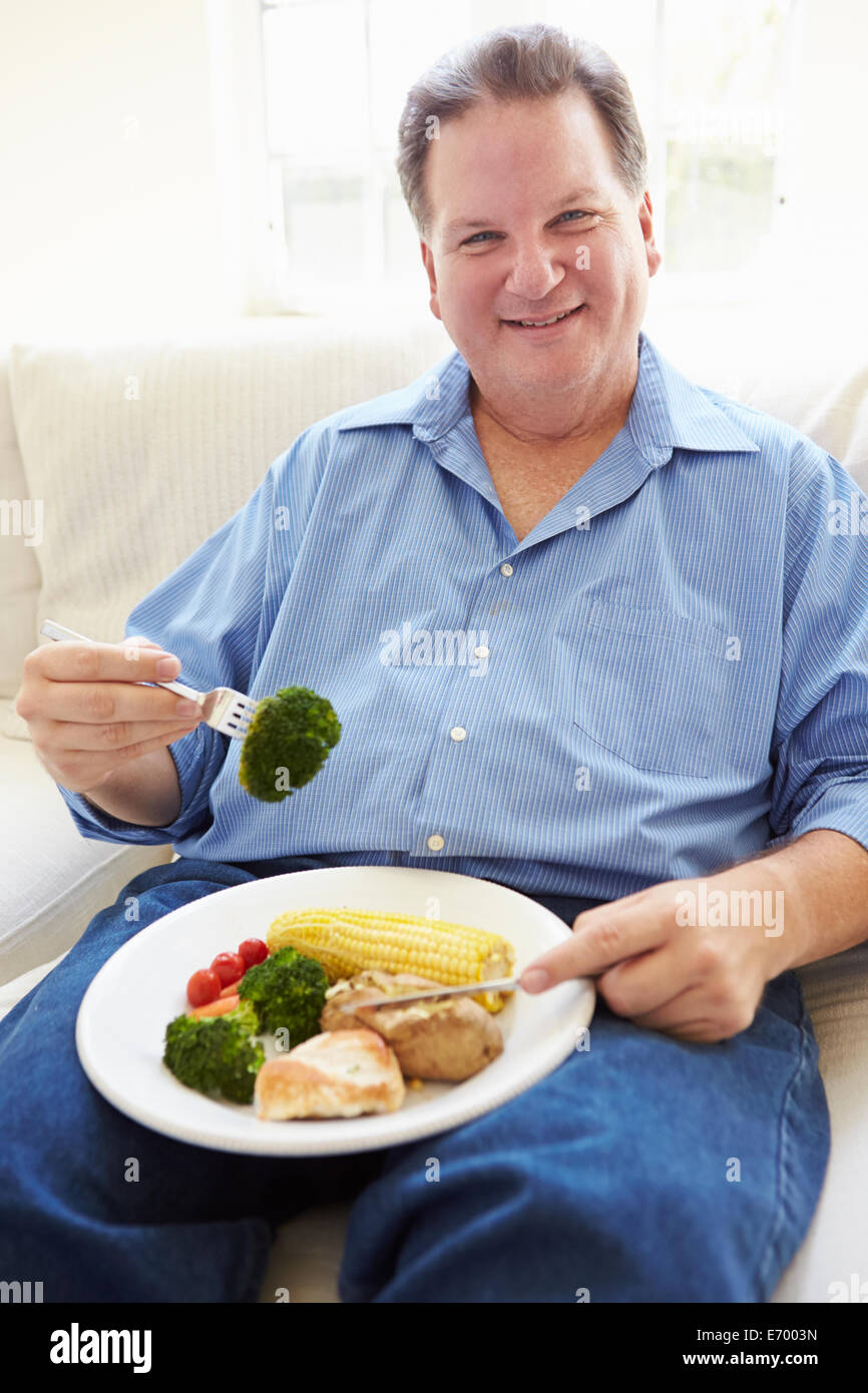 Il sovrappeso uomo mangiare sano pasto seduti sul divano Foto Stock