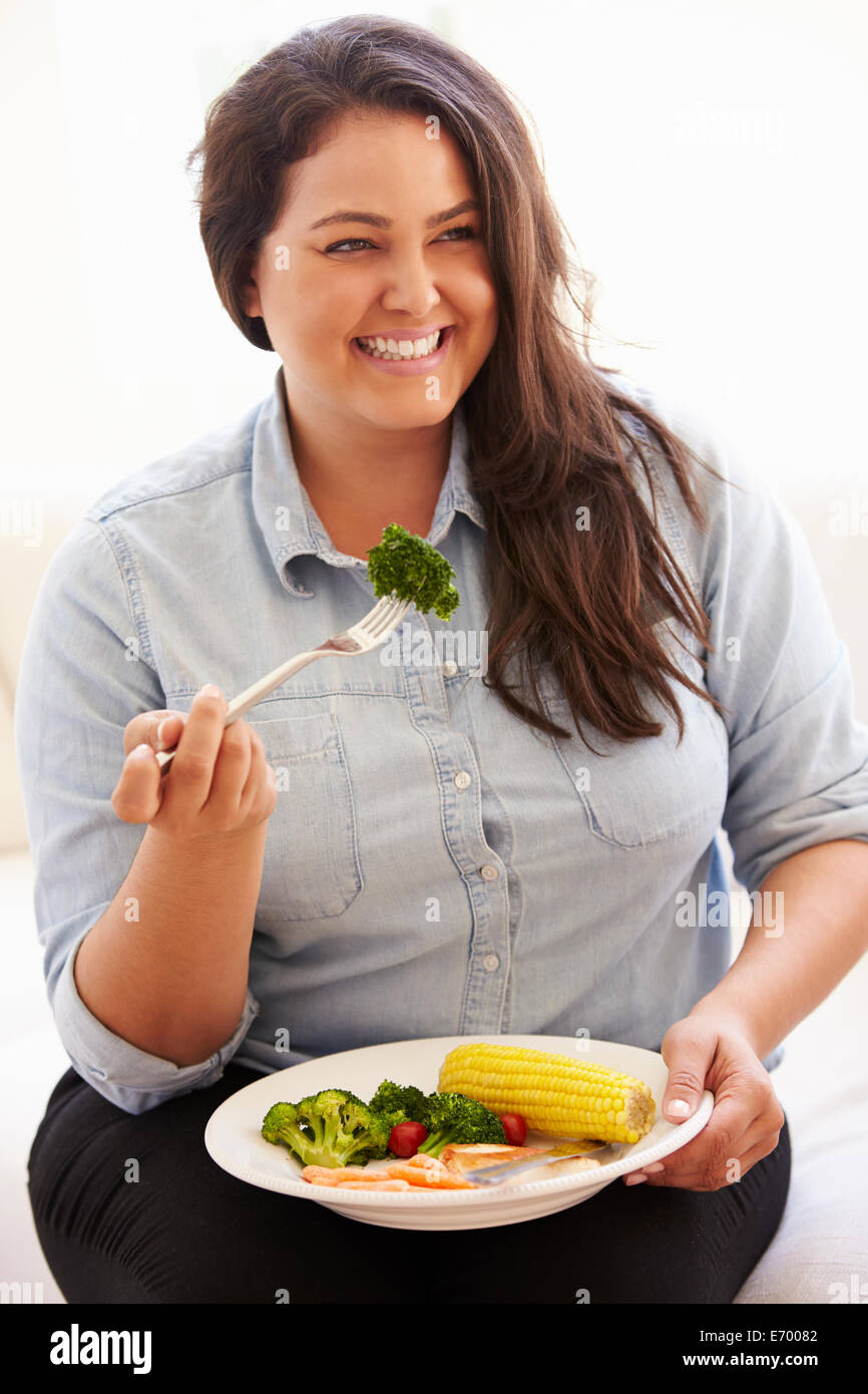 Donna sovrappeso mangiare sano pasto seduti sul divano Foto Stock