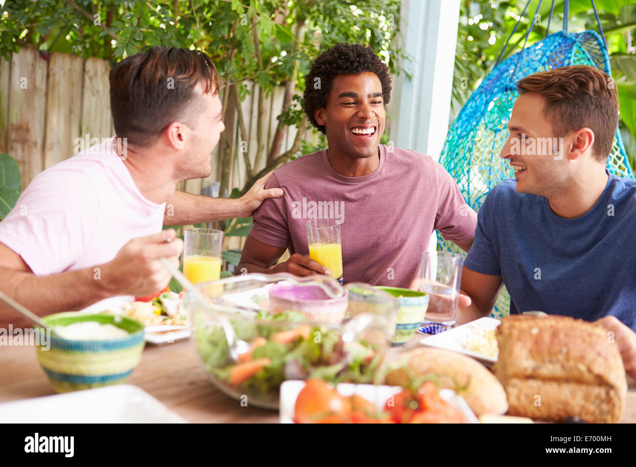 Tre amici maschi godendo di pasto all'aperto a casa Foto Stock