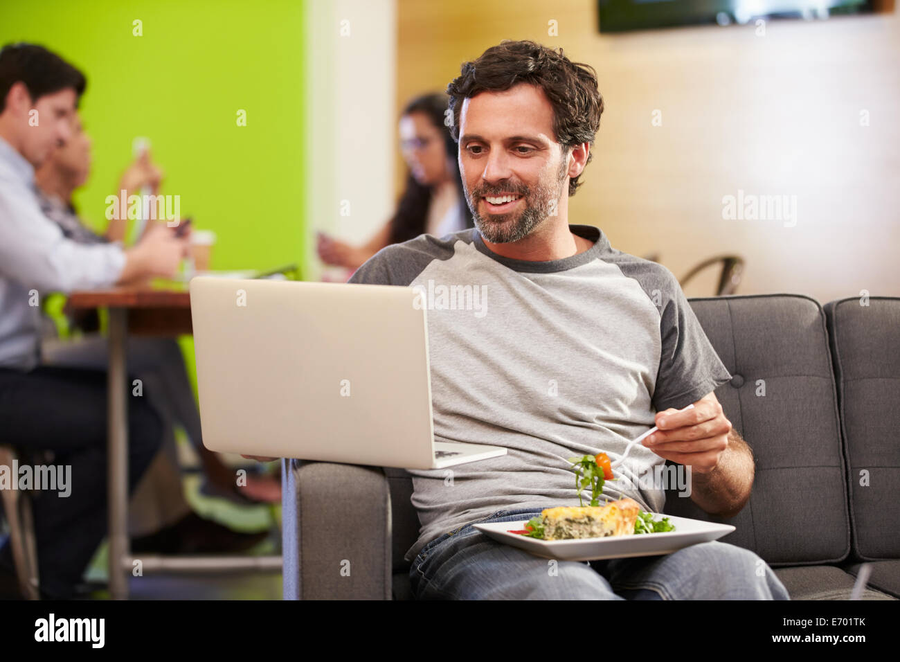 Uomo seduto sul divano e mangiare il pranzo in Design Studio Foto Stock