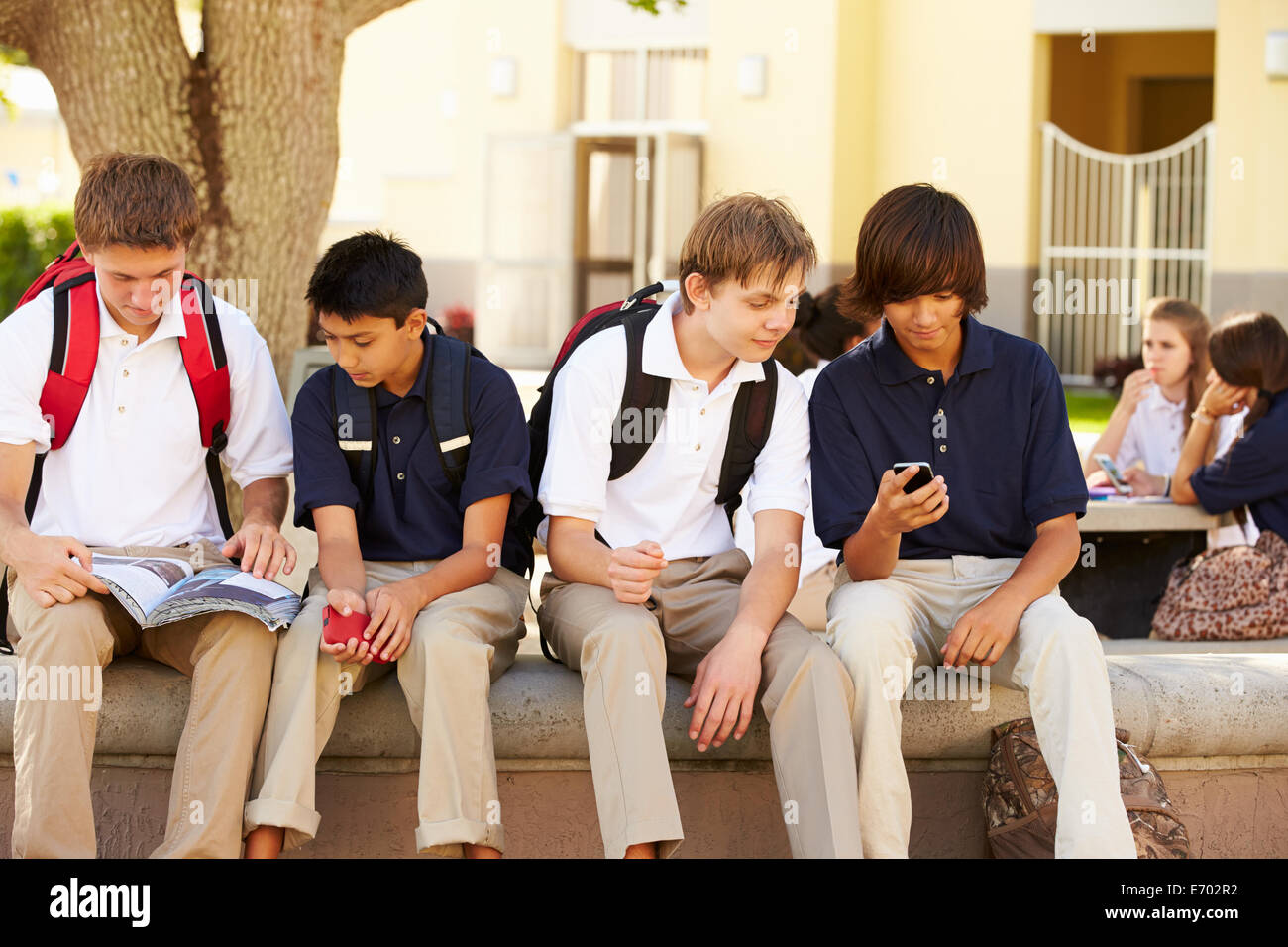 Maschio di alta scuola gli studenti utilizzando i telefoni cellulari sul campus della scuola Foto Stock