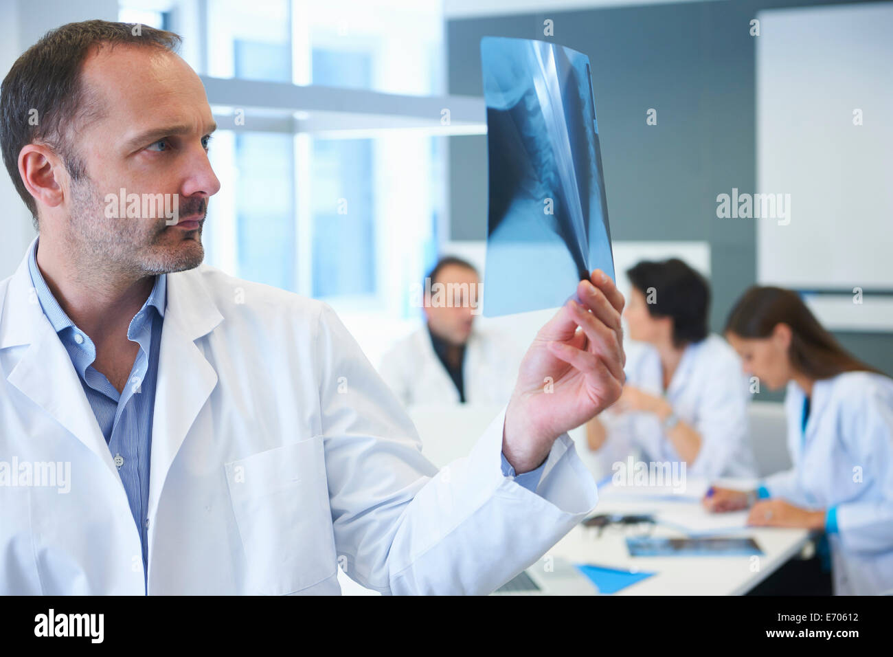 Medico maschio guardando a raggi x e i colleghi avendo discussioni dietro Foto Stock