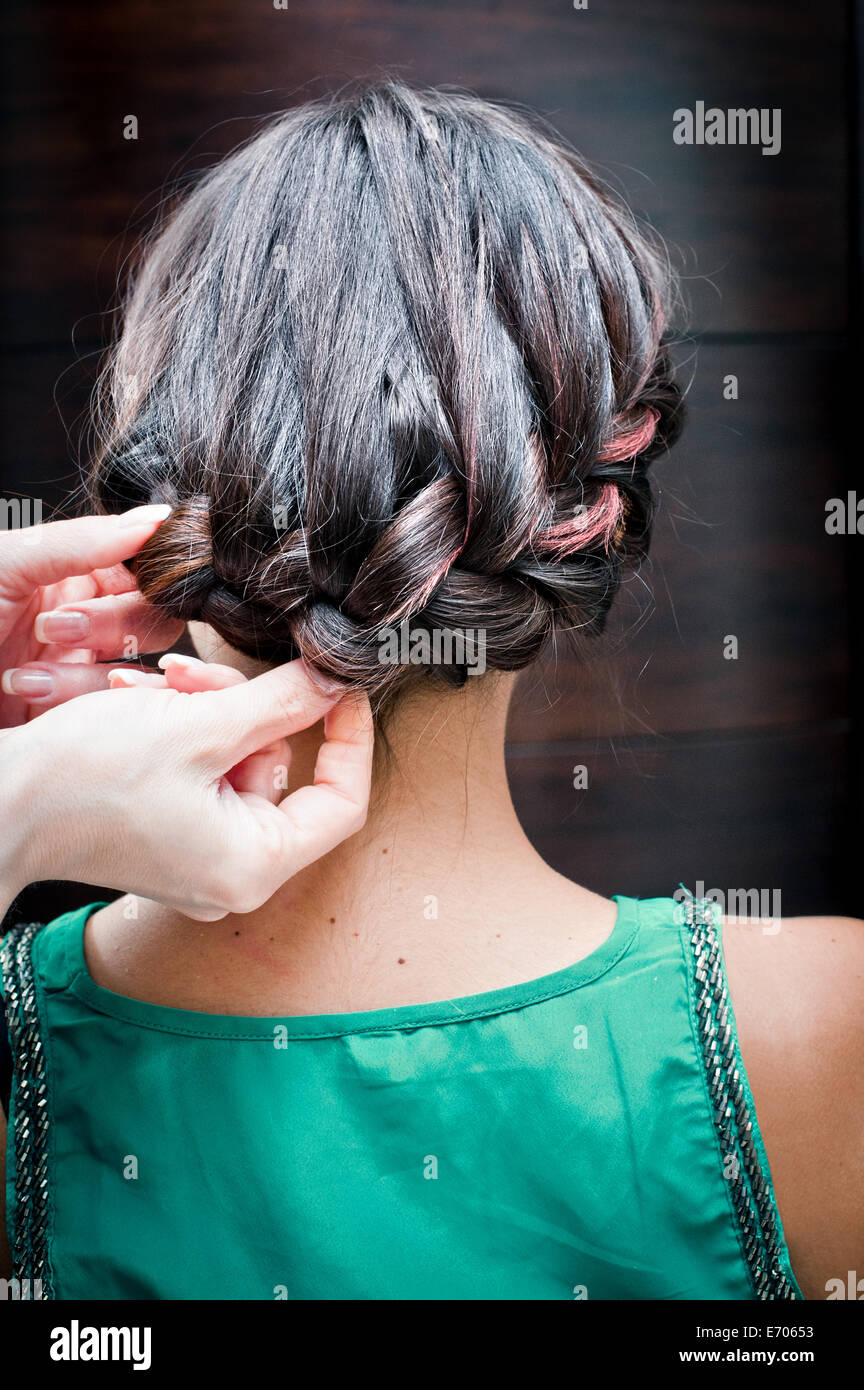 Vista posteriore del parrucchiere femminile intreccio di giovane donna capelli nel salone di parrucchiere Foto Stock