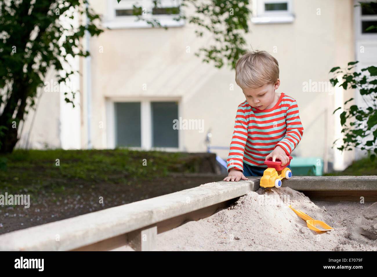 Bimbi maschio spingendo giocattolo auto nella buca di sabbia in giardino Foto Stock