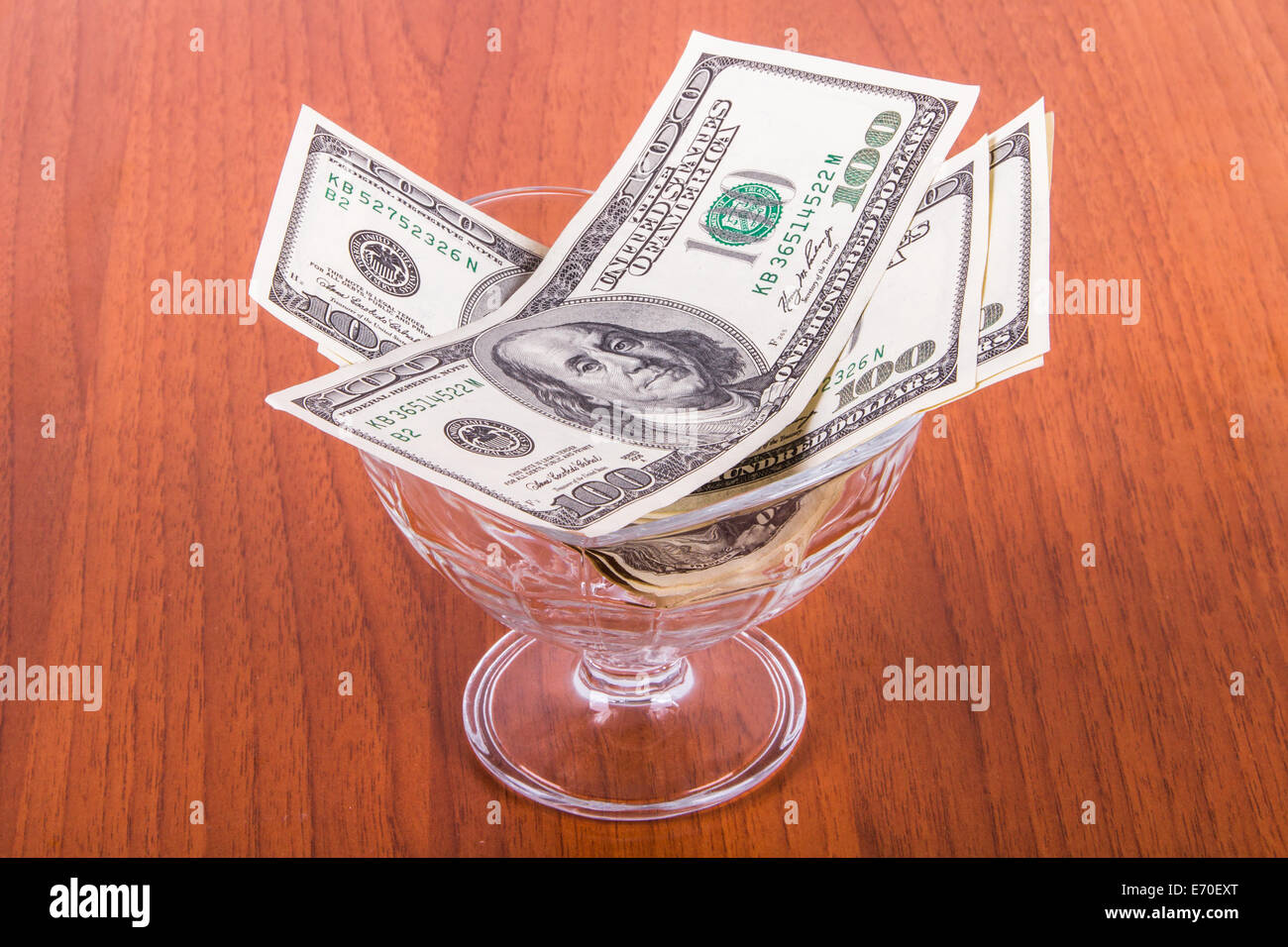 Un centinaio di dollari di banconote in recipiente di vetro su un tavolo di legno. Foto Stock