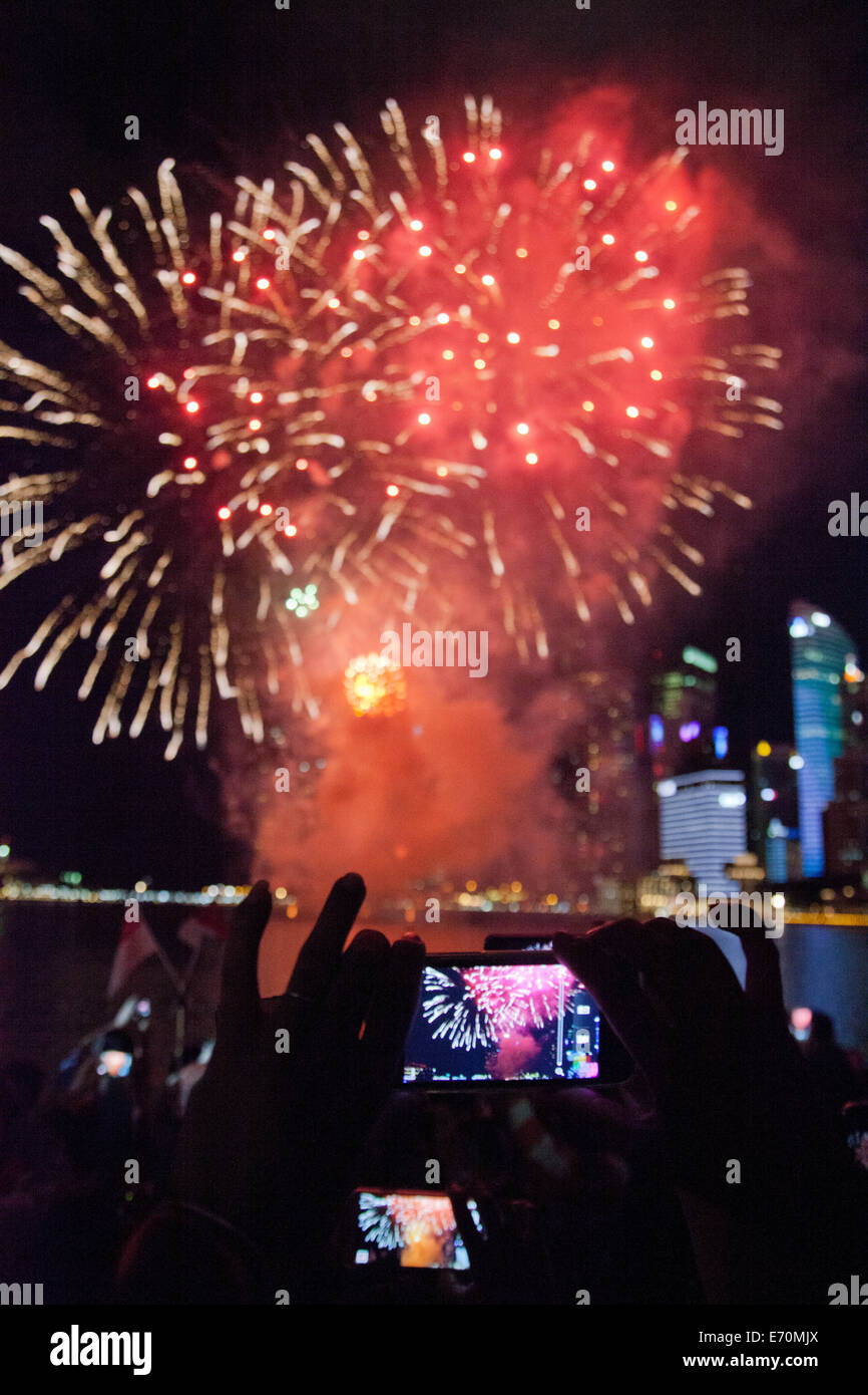 Festaioli catturare il Giorno di Indipendenza fuochi d'artificio celebrazioni nei loro telefoni cellulari e tablet presso la Baia di Singapore Foto Stock