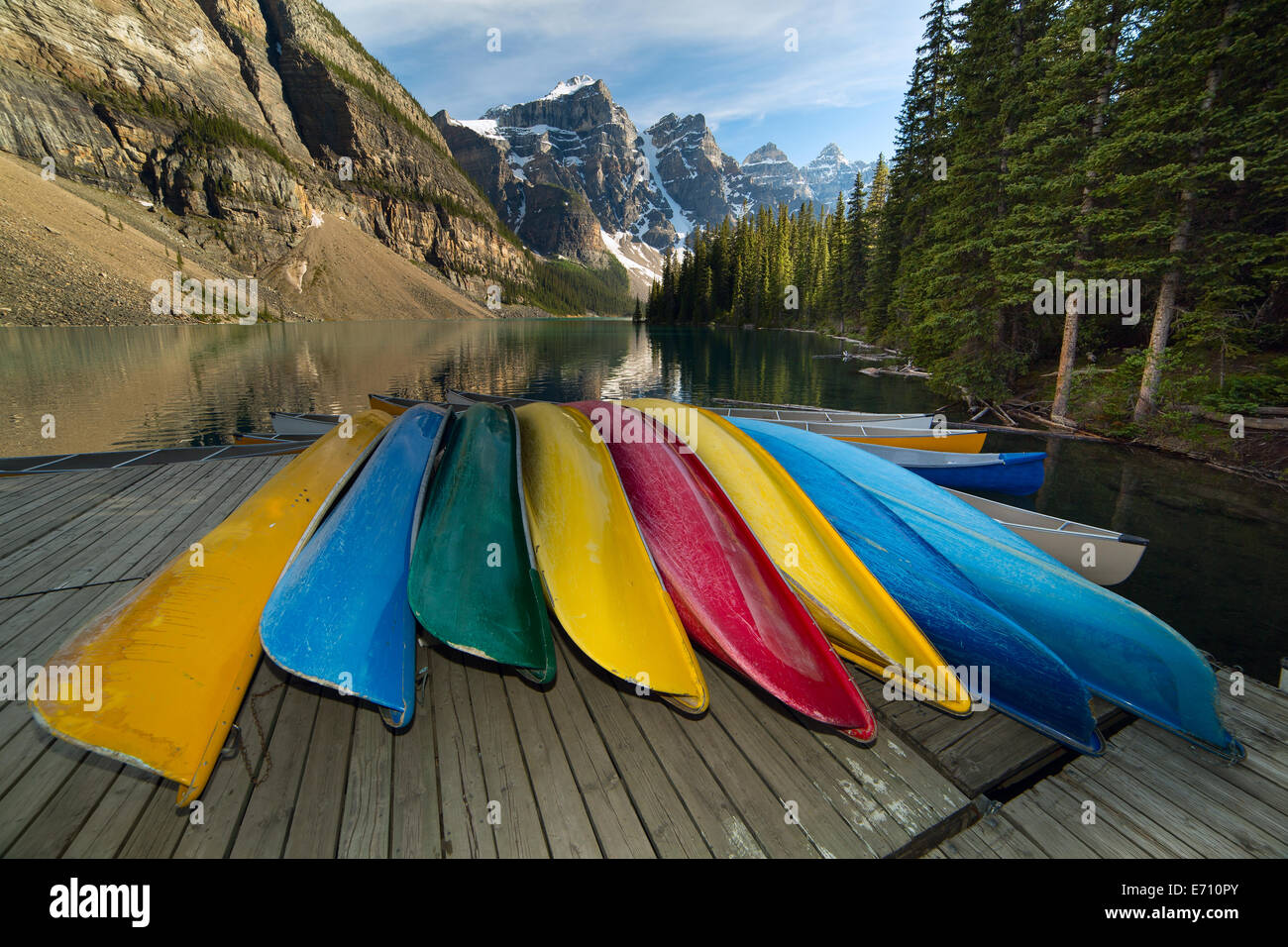 Colorato di canoe sul ponte di legno da un lago di montagna con scogliere in background Foto Stock