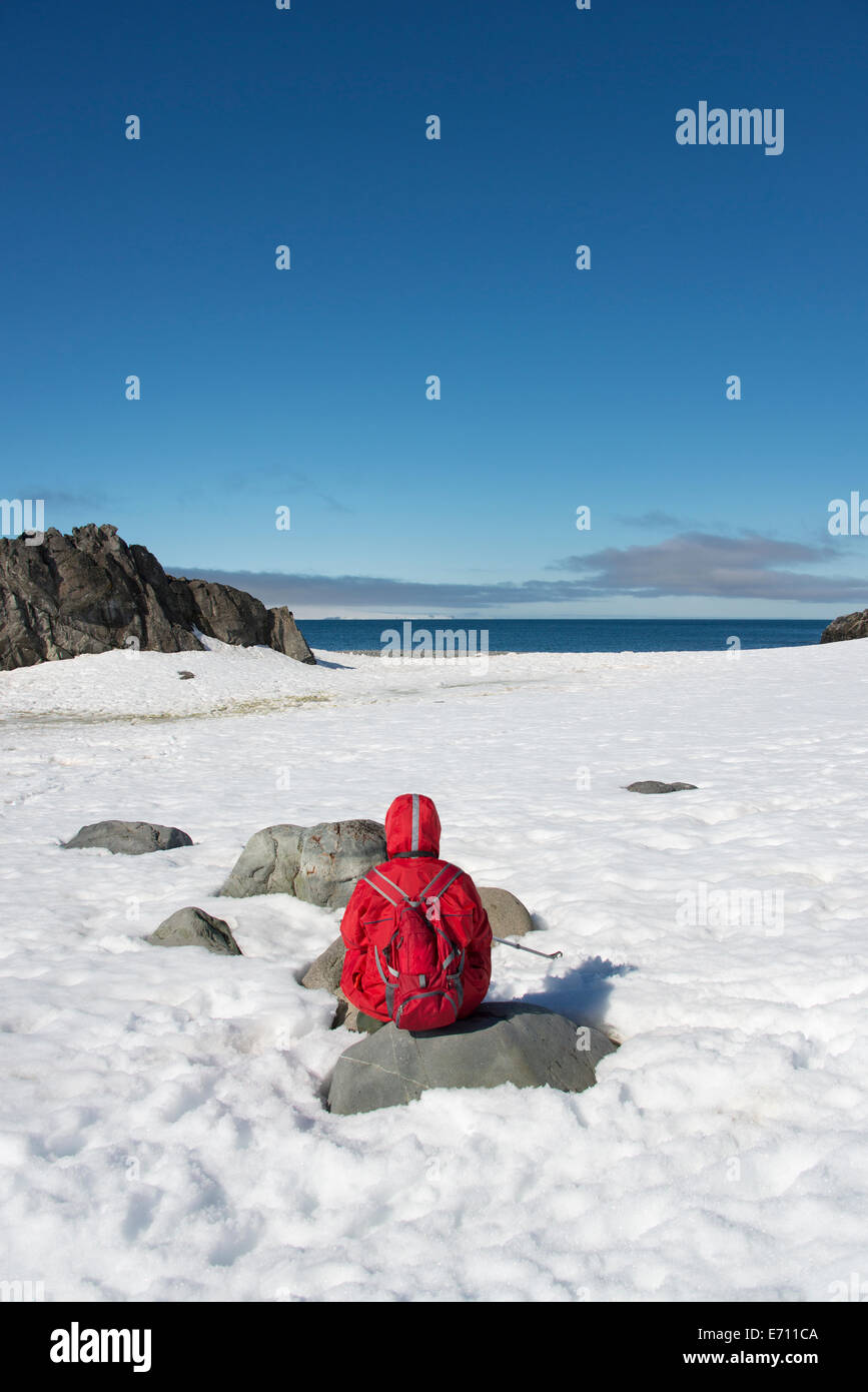 Una persona in una giacca arancione seduto tenendo nel paesaggio su un isola antartico. Foto Stock