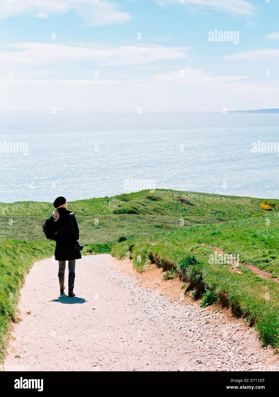 Una donna in piedi su un percorso sulla scogliera che guarda al mare. Foto Stock