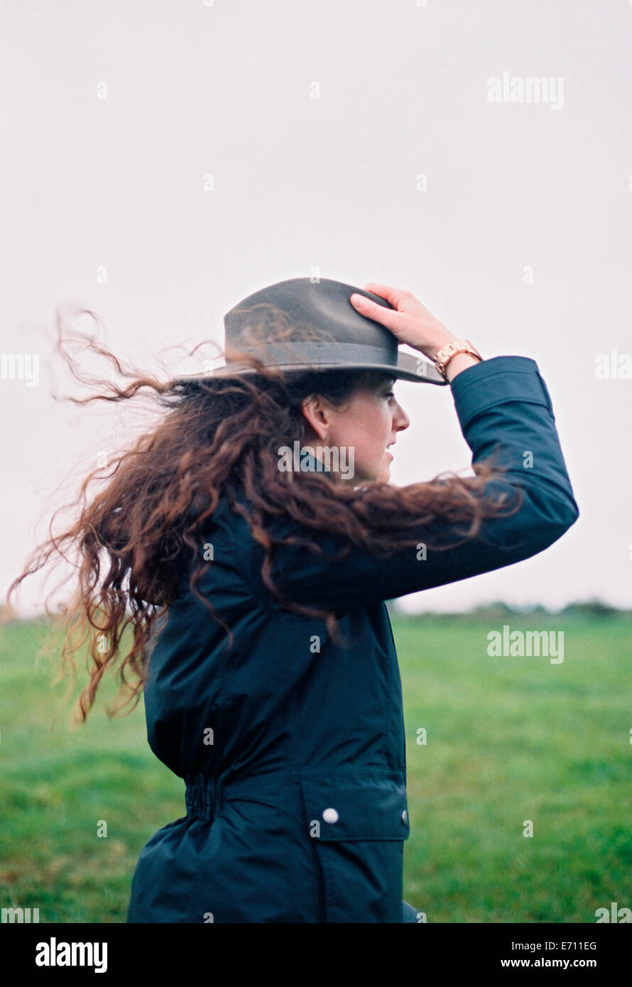 Una donna con capelli lunghi viene soffiato nel vento, tenendo il suo  cappello Foto stock - Alamy