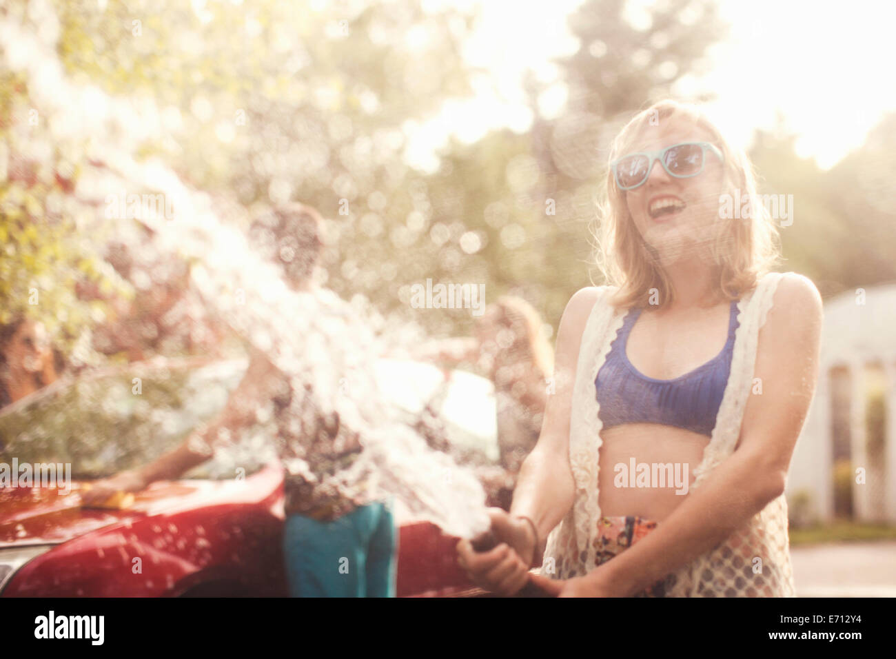 Giovane donna la spruzzatura di acqua dal tubo flessibile Foto Stock