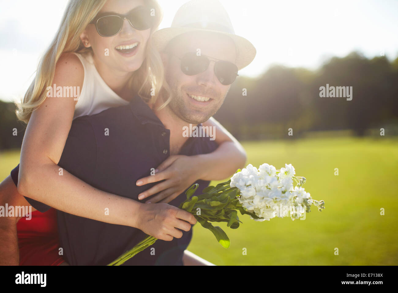 Giovane Donna con fiori getting piggy back da ragazzo nel parco Foto Stock