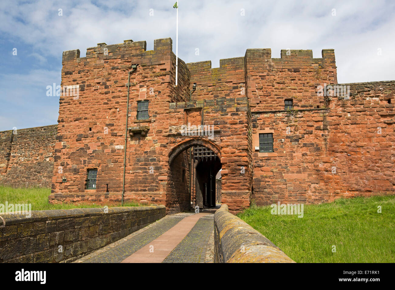 La storica Carlisle Castle con imponenti muri in arenaria rossa, ingresso con portcullis,e fossato erboso sotto il cielo blu Foto Stock