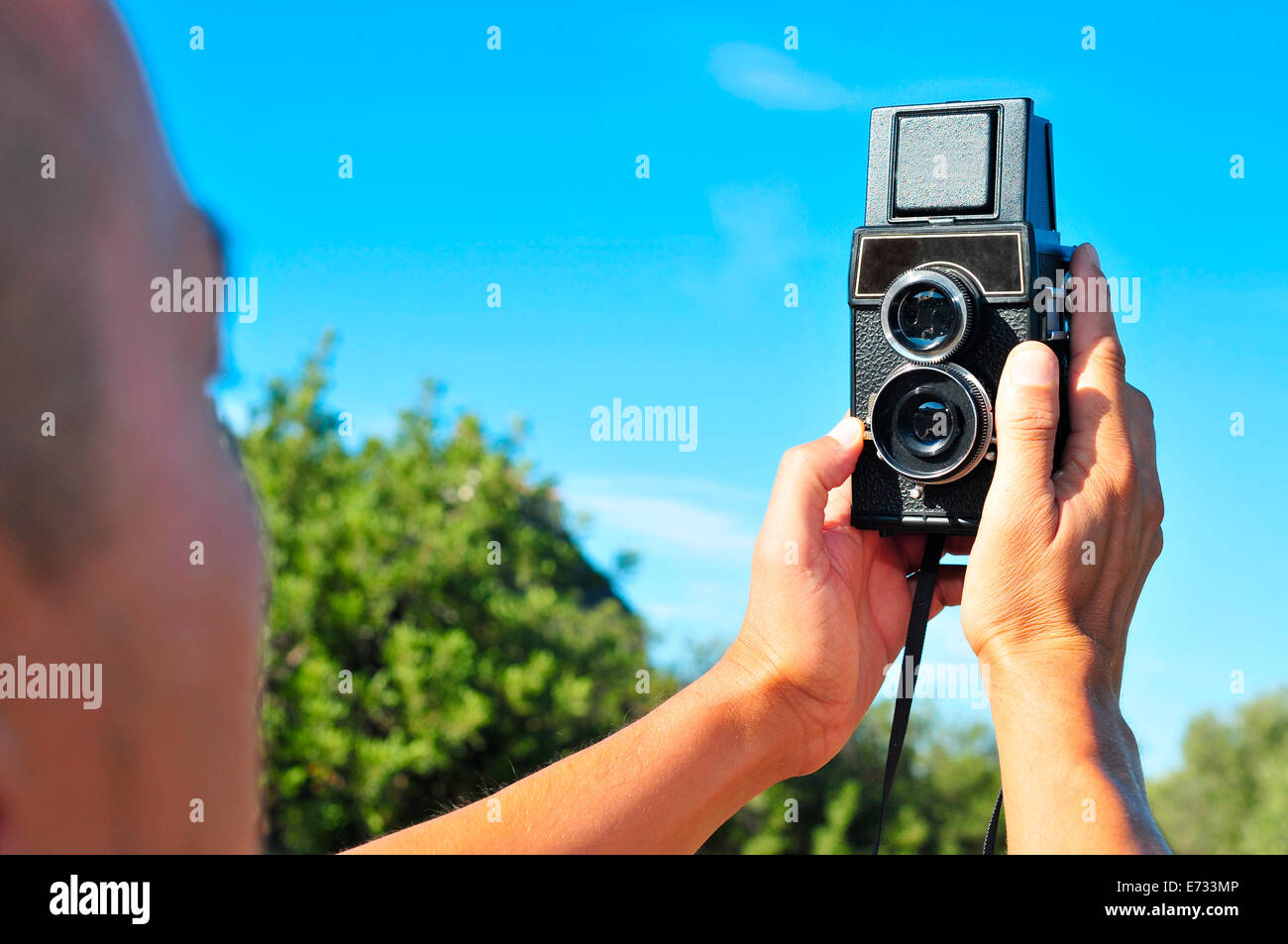 Primo piano di un giovane uomo prendendo un selfie con una vecchia fotocamera medio formato in uno scenario naturale Foto Stock