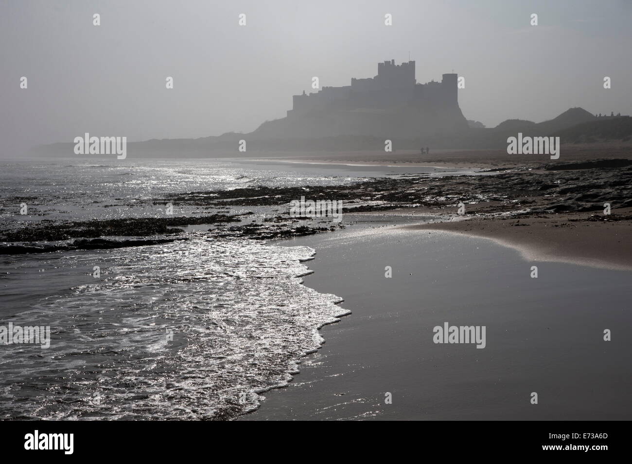 Onde che si infrangono a spiaggia Bamburgh guardando verso il castello di Bamburgh in una nebbiosa mattina, Northumberland, England, Regno Unito Foto Stock