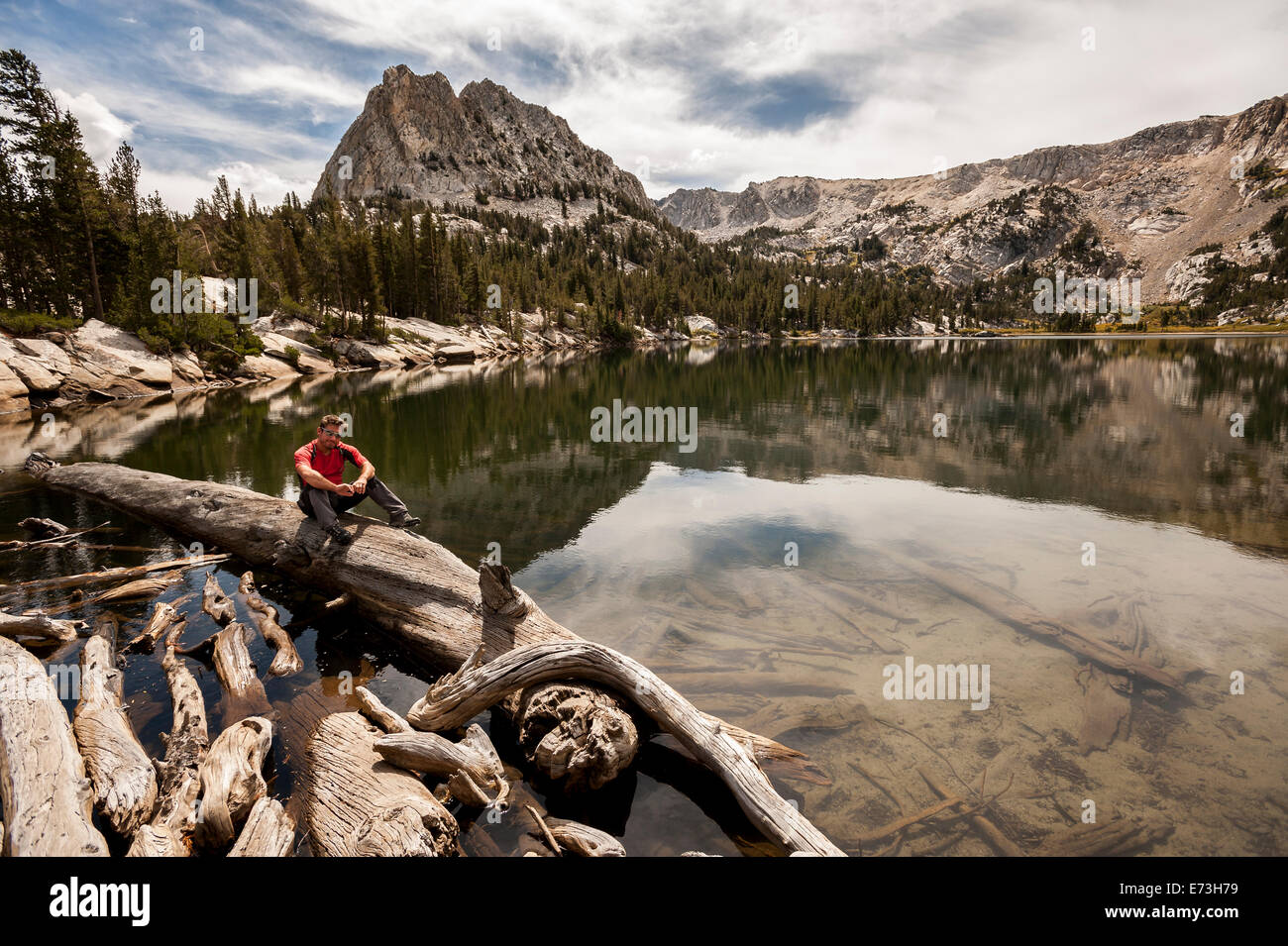 Ragazzo seduto su un tronco di albero sul bordo di un lago di montagna in Mammoth Lakes, California. Foto Stock