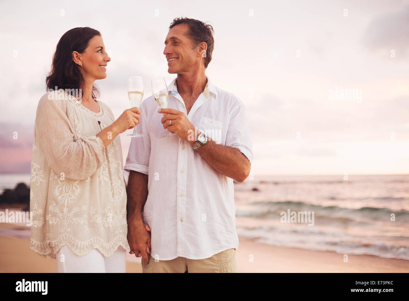 Romantica felice Coppia Matura bevendo champagne sulla spiaggia al tramonto. Vacanze viaggi pensionamento celebrazione dell anniversario. Foto Stock