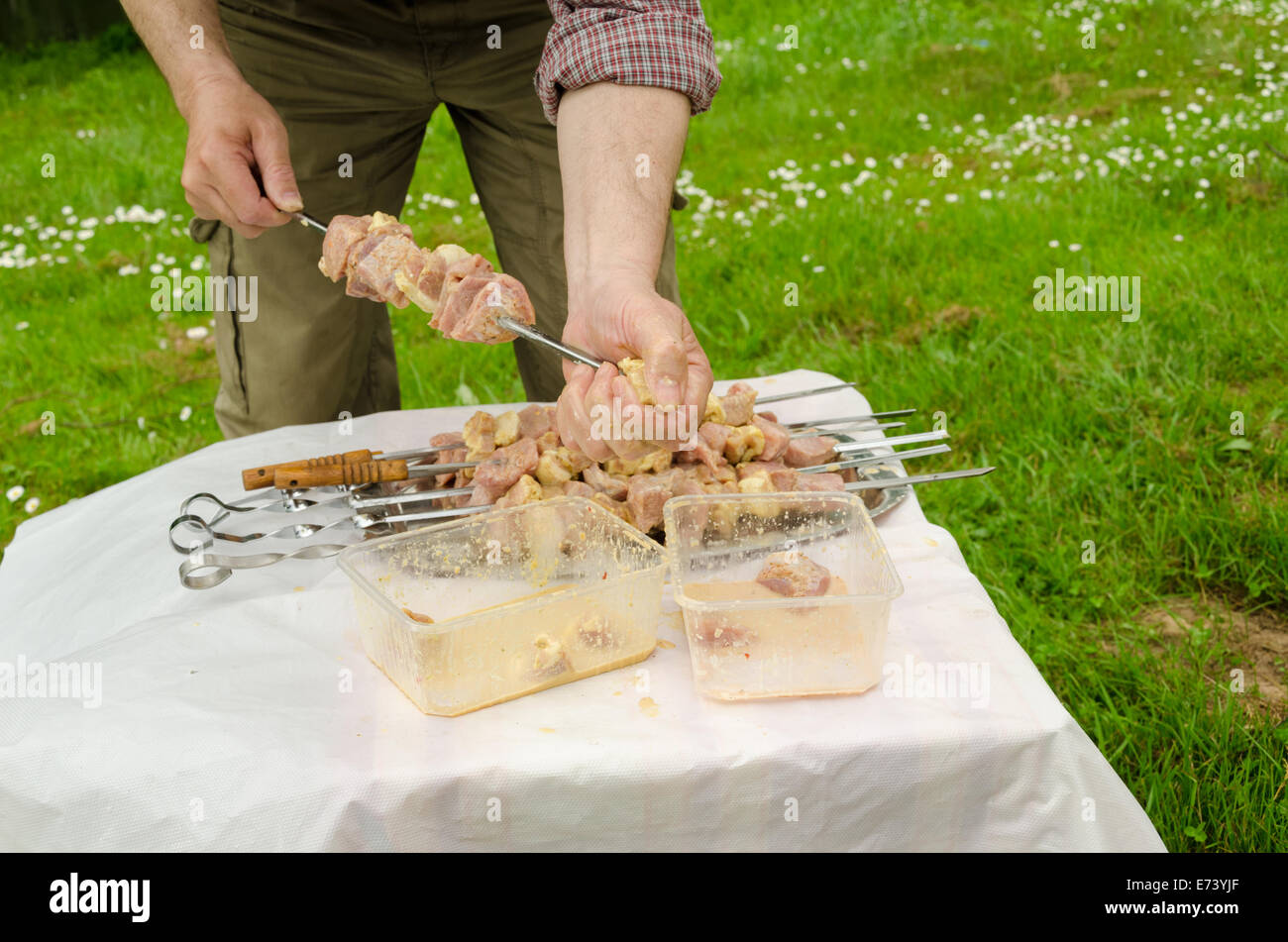 L'uomo messo ordinatamente verde infilza carne di maiale preparato per la cottura a fuoco Foto Stock