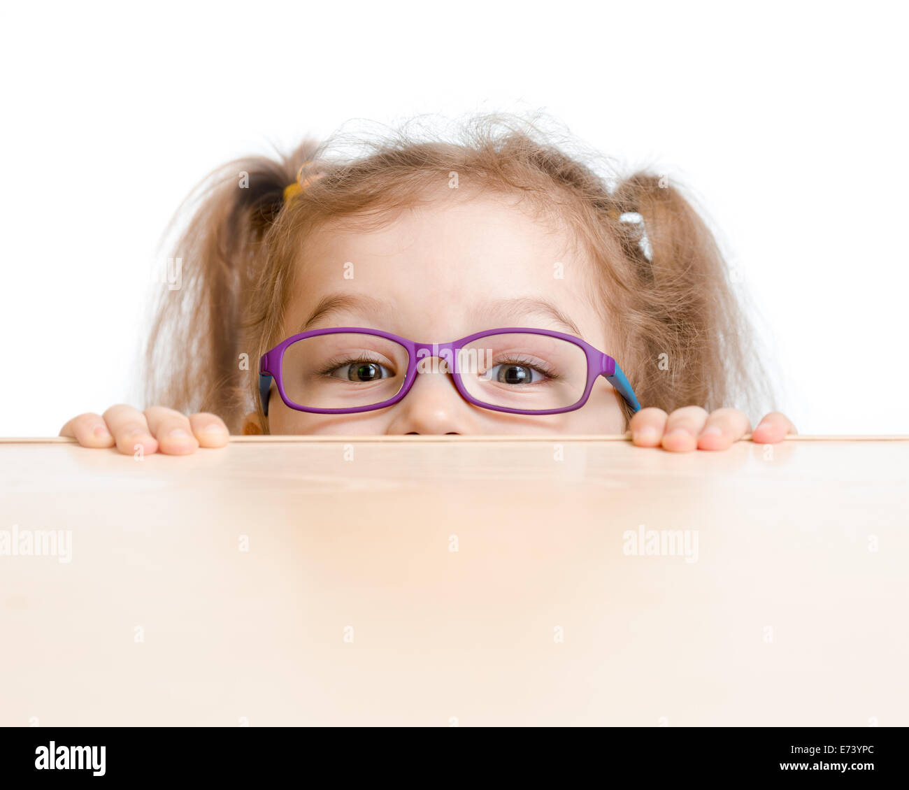 Funny Girl in occhiali nascondendo dietro un tavolo Foto Stock