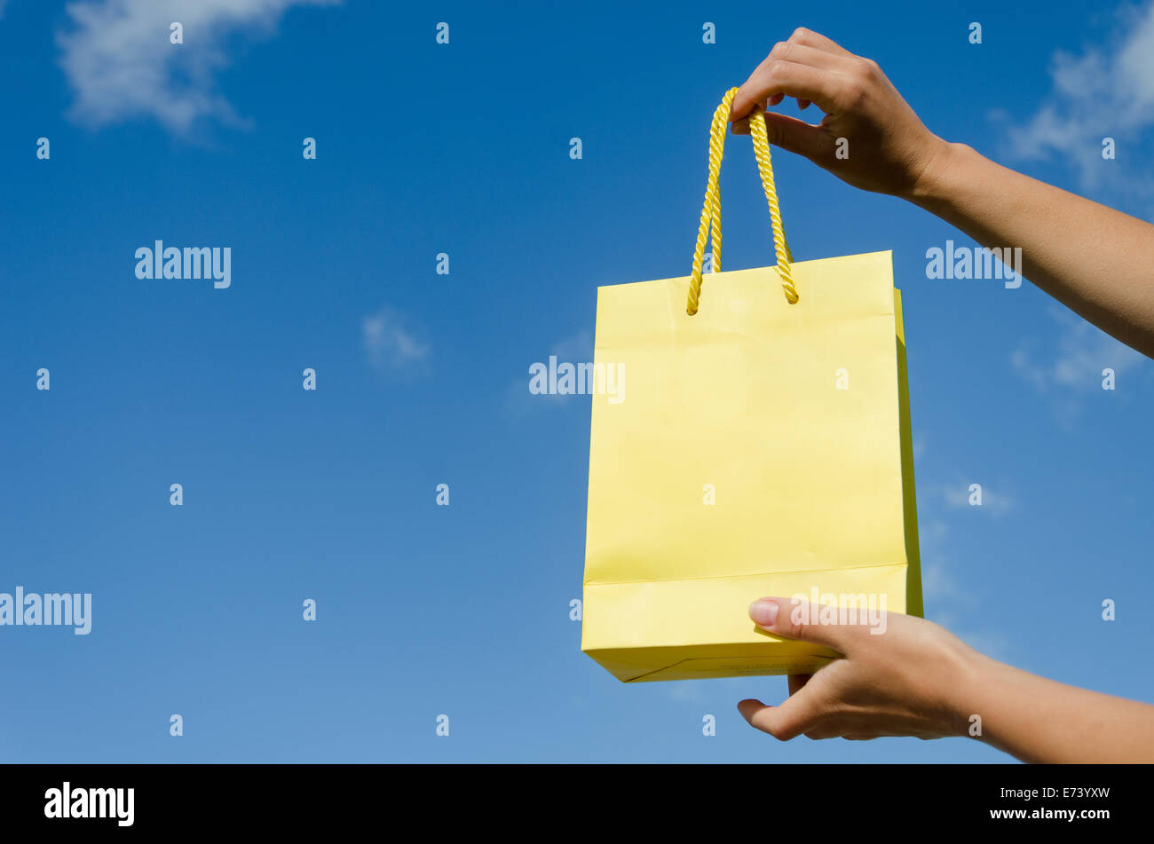 Donna tenere in mano la carta gialla borsa regalo sul cielo blu sullo sfondo Foto Stock