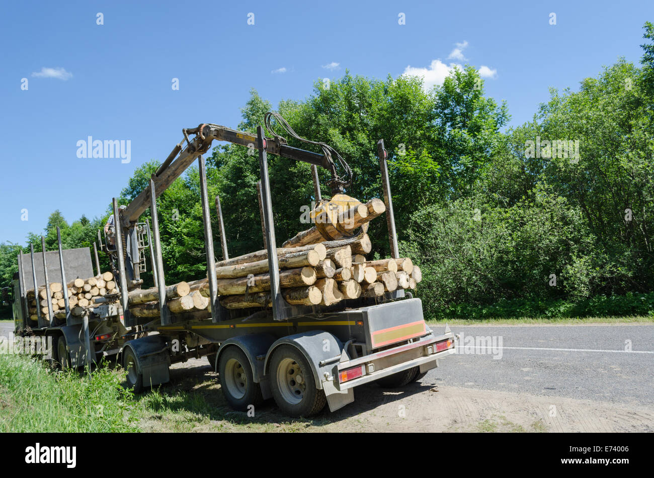 Foresta di pesanti macchinari con rimorchio log tagliato palo stand lungo la strada di ghiaia Foto Stock