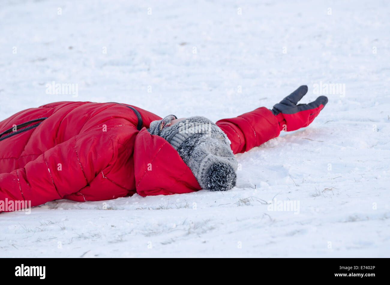 Bambino giacciono sulla neve con il rosso Caldo giubbotto in piuma stanco dalla slitta all'aperto, inverno tempo libero Foto Stock