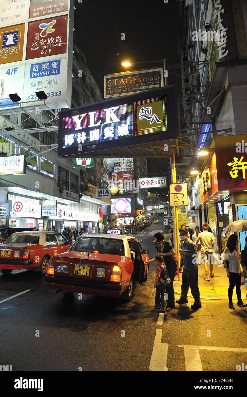 Tempo di notte scena di strada, con la famiglia imbarco taxi. Kowloon, Hong Kong, Cina Foto Stock