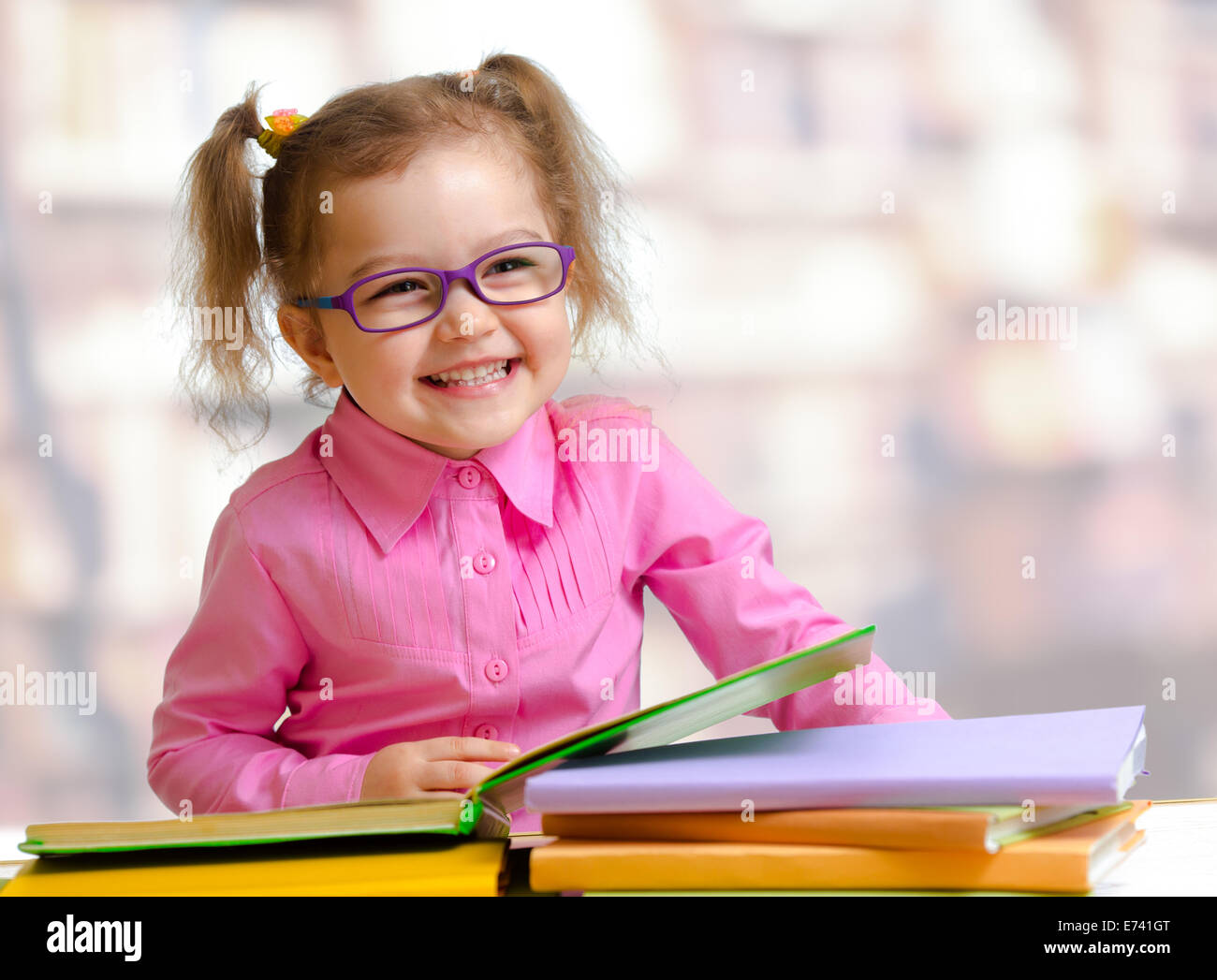 Bambino felice ragazza in occhiali lettura di libri seduta a tavola Foto Stock
