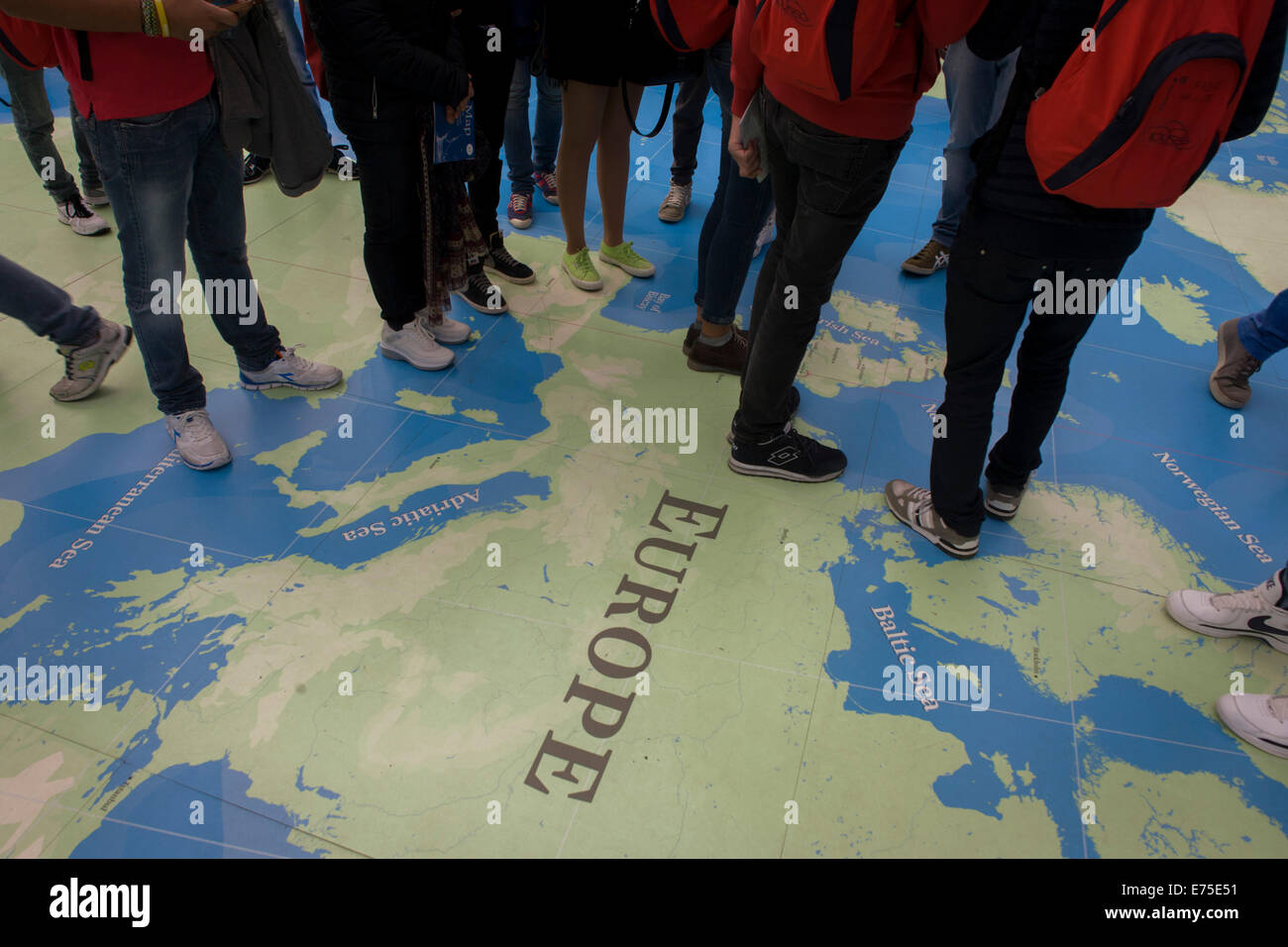 Le gambe e i piedi di studenti stranieri in piedi sopra l'Europa su una mappa del mondo presso il National Maritime Museum di Greenwich. Foto Stock