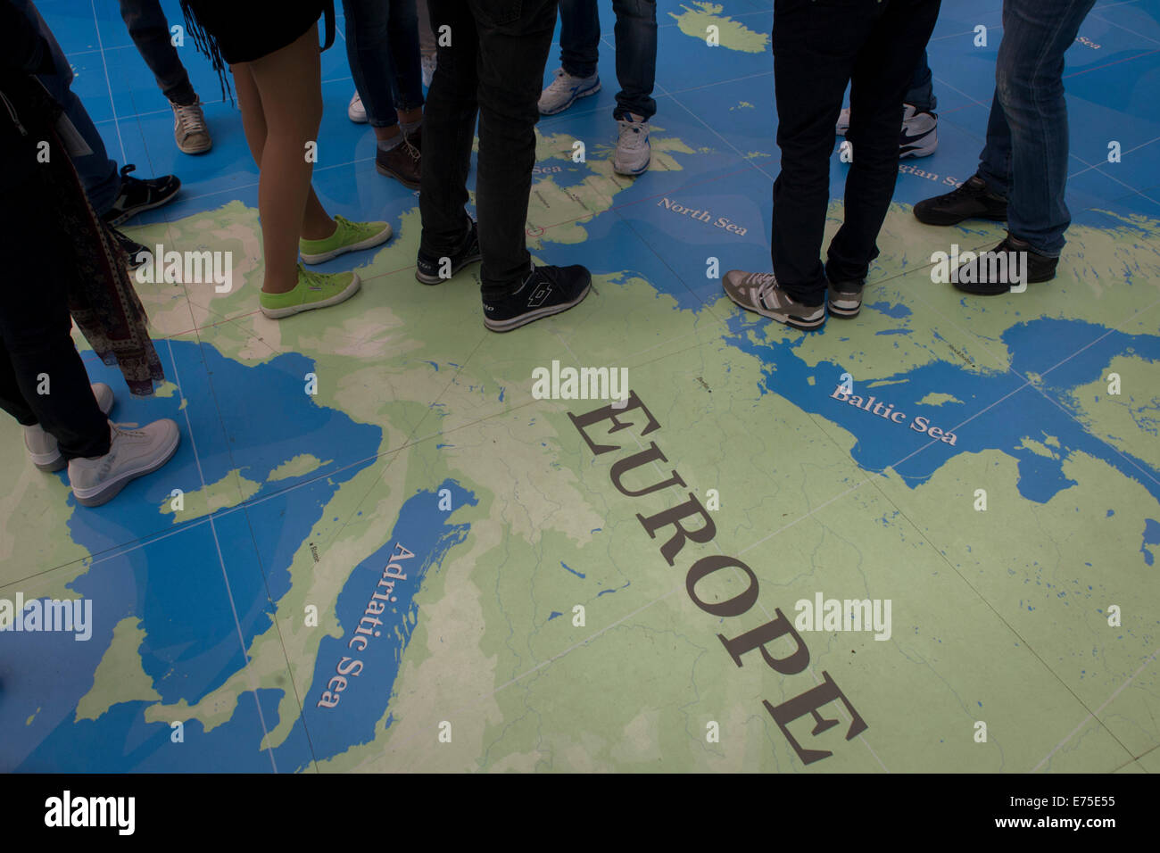 Le gambe e i piedi di studenti stranieri in piedi sopra l'Europa su una mappa del mondo presso il National Maritime Museum di Greenwich. Foto Stock