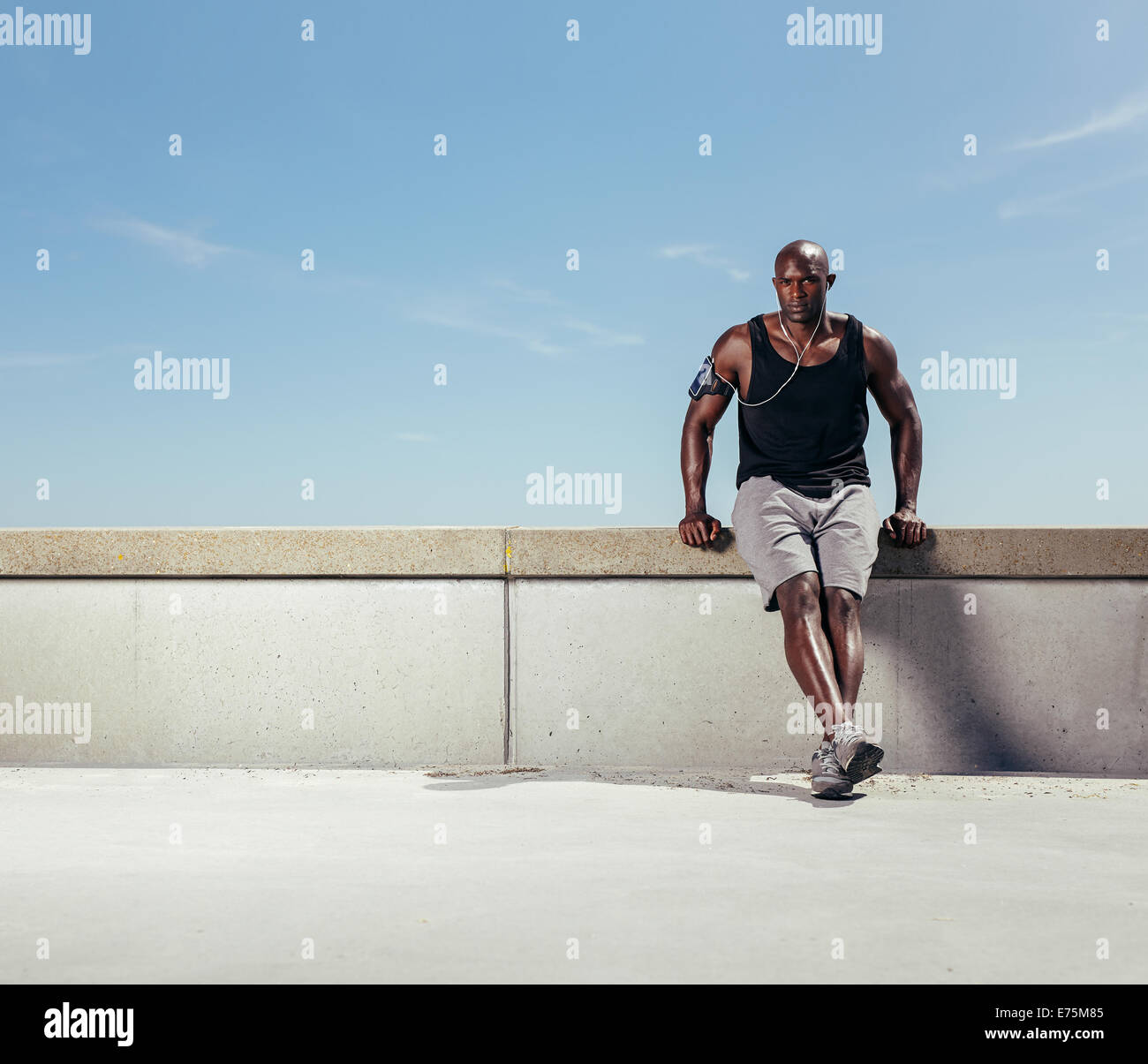 Immagine di montare il giovane uomo rilassante sul terrapieno dopo la sua esecuzione contro il cielo blu. Africa atleta maschio all aperto con copyspace. Foto Stock