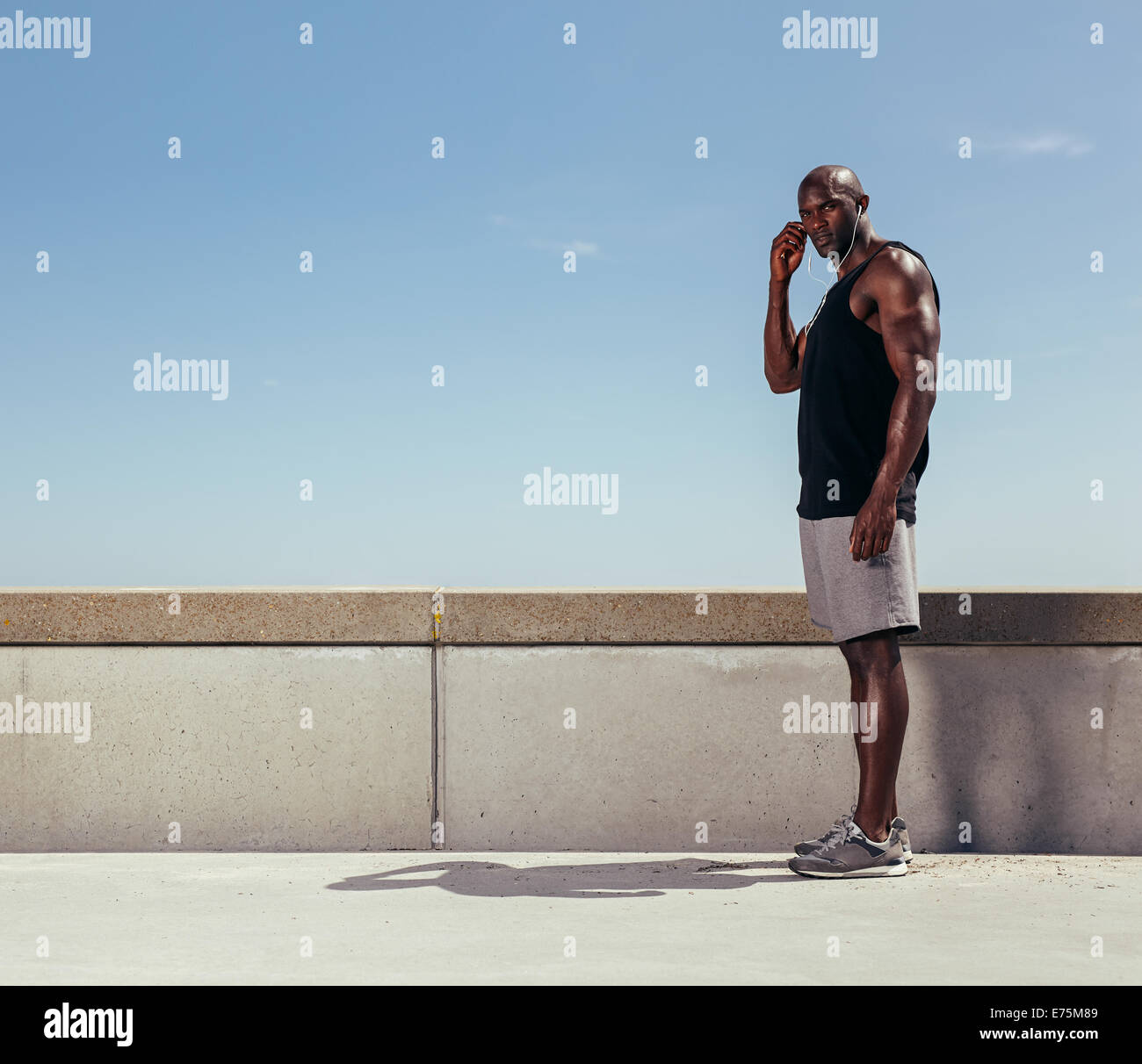 Ritratto di montare il giovane uomo in piedi su un marciapiede guardando la fotocamera. Africa modello fitness indossa gli auricolari. Foto Stock