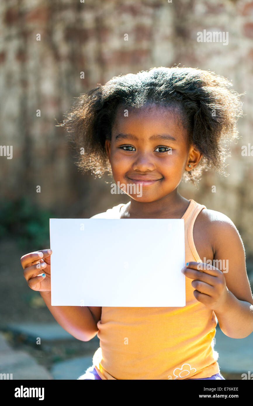 Ritratto di poco ragazza africana che mostra vuoto carta bianca all'esterno. Foto Stock