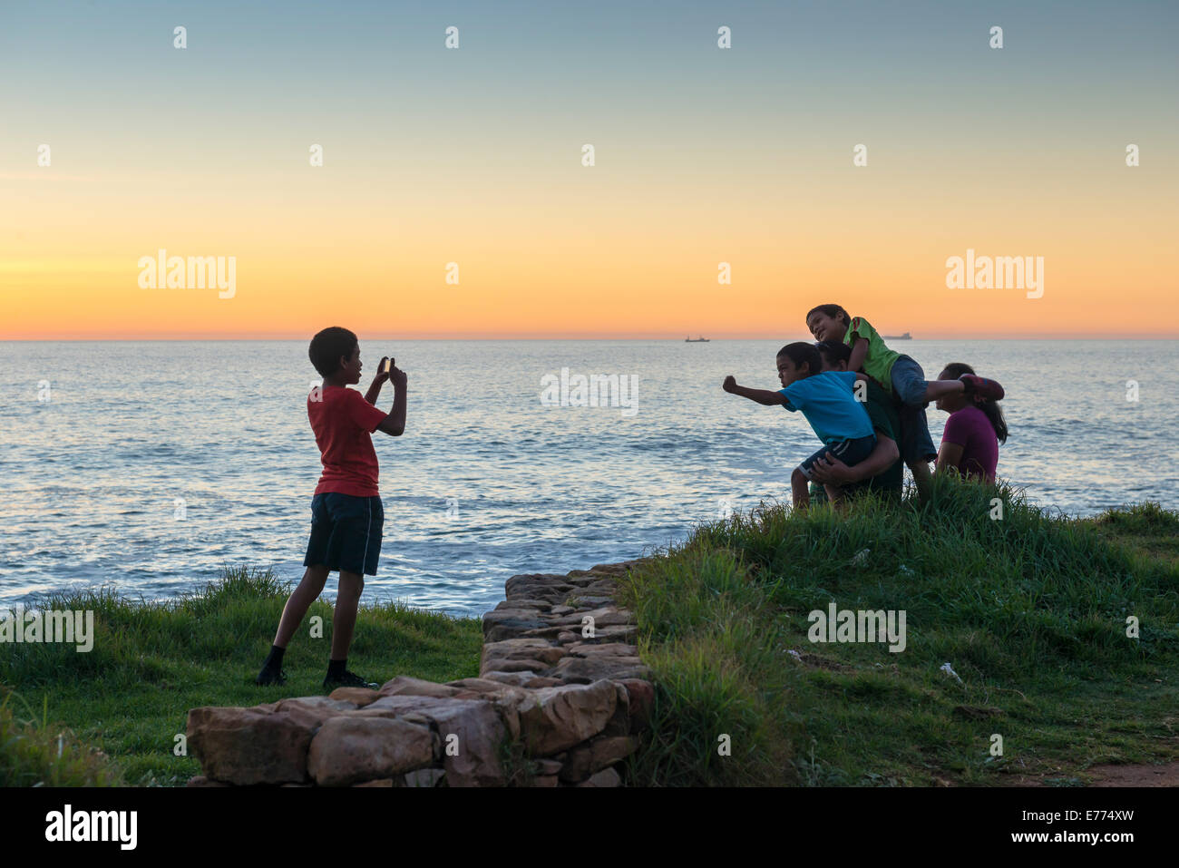 Ragazzo prende una foto dei suoi amici al tramonto sulla costa a sud di Città del Capo, Sud Africa Foto Stock