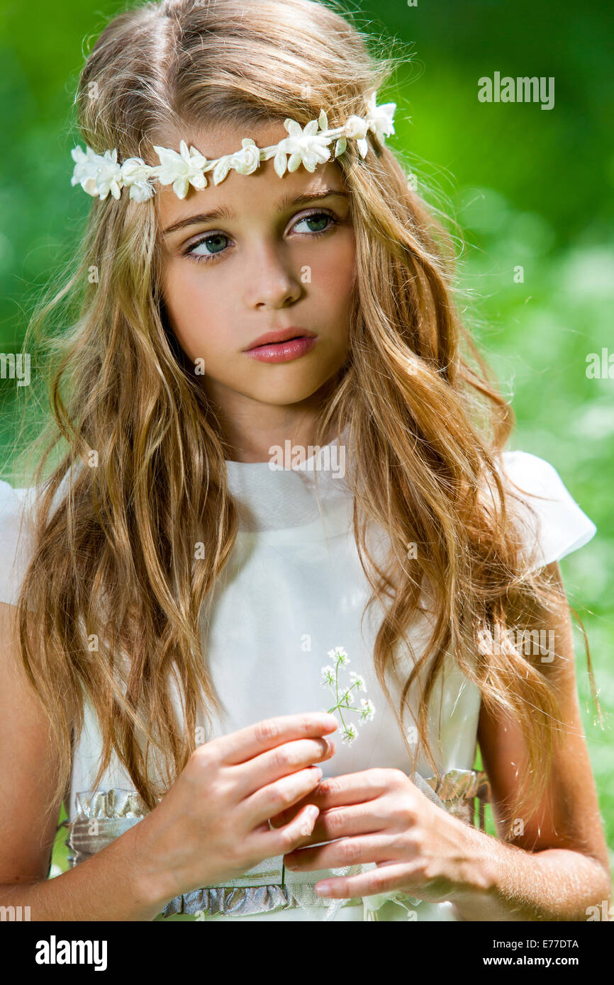 Close up ritratto della cute girl in abito bianco azienda fiore all'esterno. Foto Stock