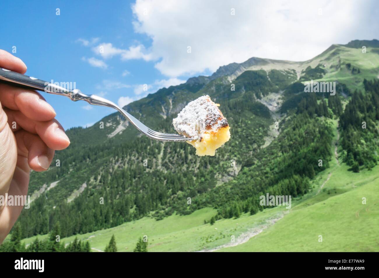 Pezzo di dolci austriaci uova strapazzate specialty ' Kaiserschmarrn ', presa con una forcella con le montagne sullo sfondo. Foto Stock