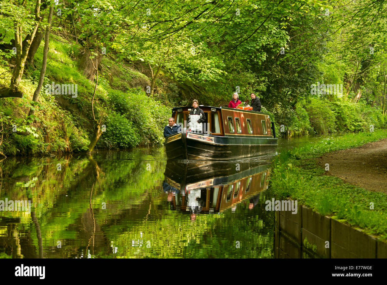 Gruppo di persone su narrowboat su Llangollen canal in Galles con la barca e circostanti boschi di smeraldo riflettono in superficie a specchio di acqua Foto Stock