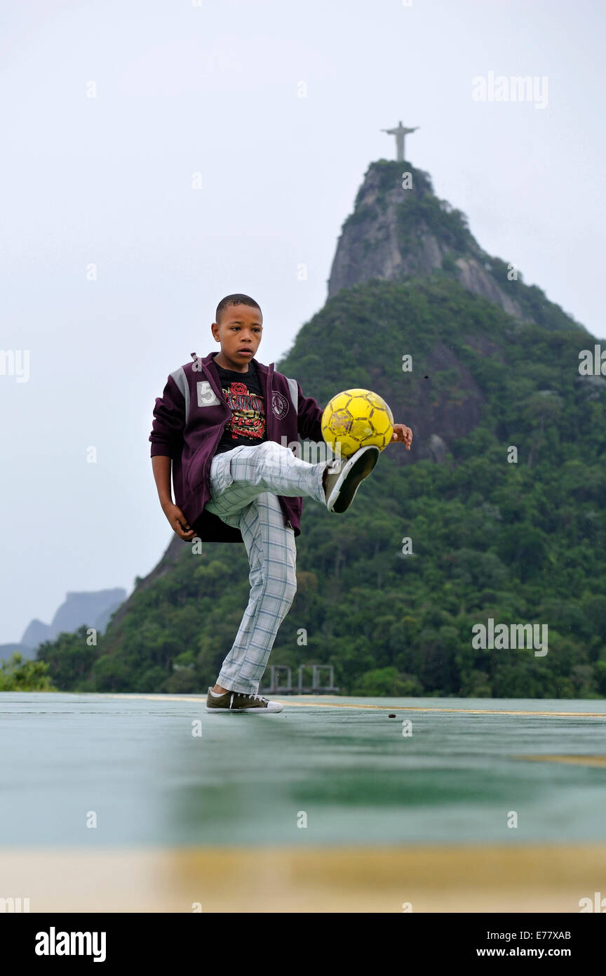 Adolescente, 15 anni, giocando con un pallone da calcio, Monte Corcovado con la statua del Cristo Redentor sul retro Foto Stock