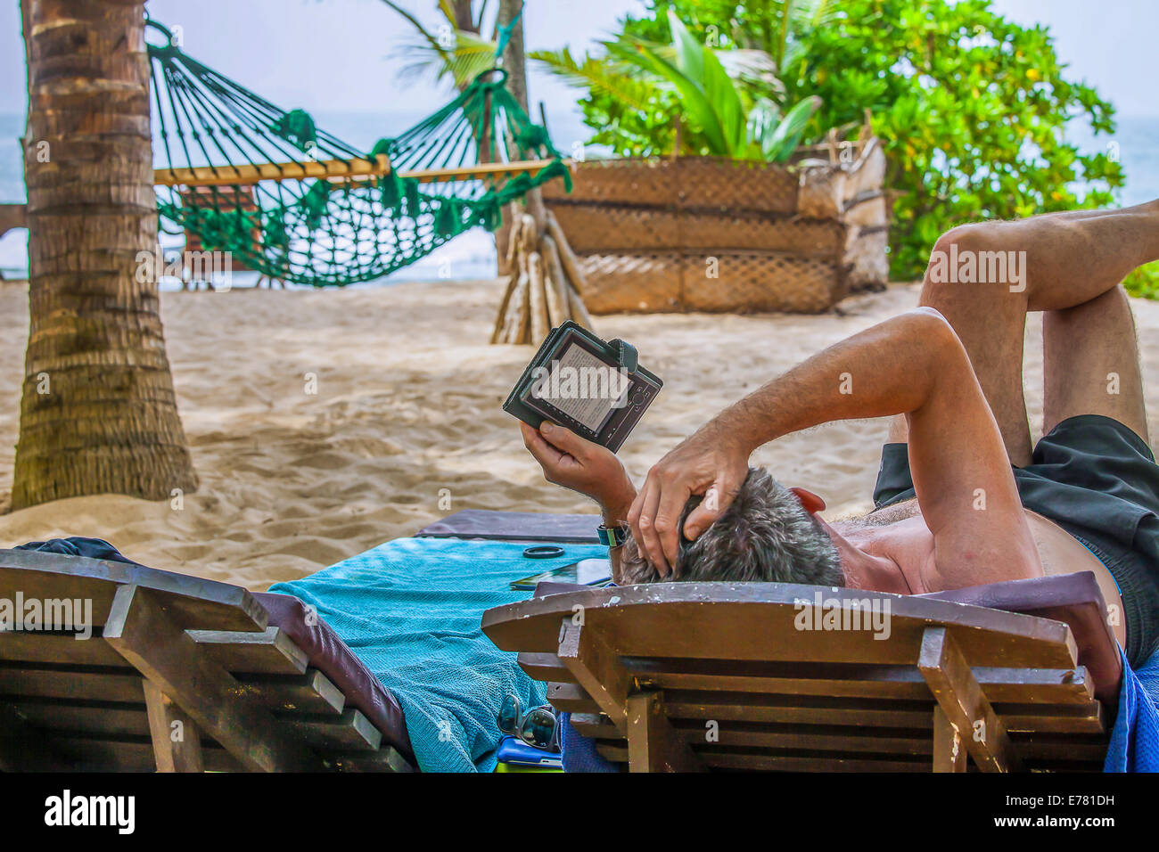 Un uomo la lettura di un e-book sulla spiaggia Foto Stock