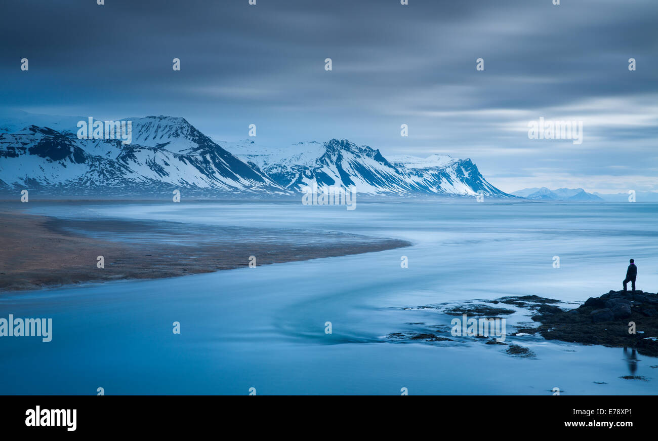 La figura solitaria di Wendy sulla costa a Budir con montagne di Holsfjall e la penisola di Snaefellsnes western Islanda Foto Stock