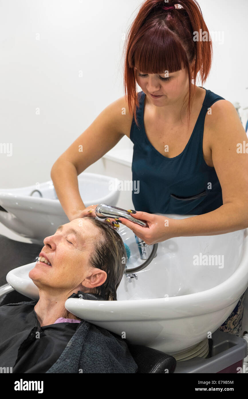 Donna anziana IN PARRUCCHIERE avente capelli lavati dal giovane partecipante parrucchiere England Regno Unito Foto Stock