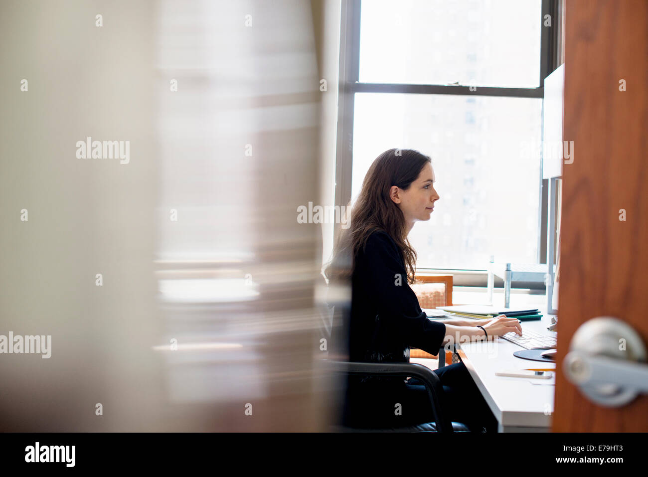 Una donna che lavora in un ufficio, seduti ad una scrivania. Foto Stock