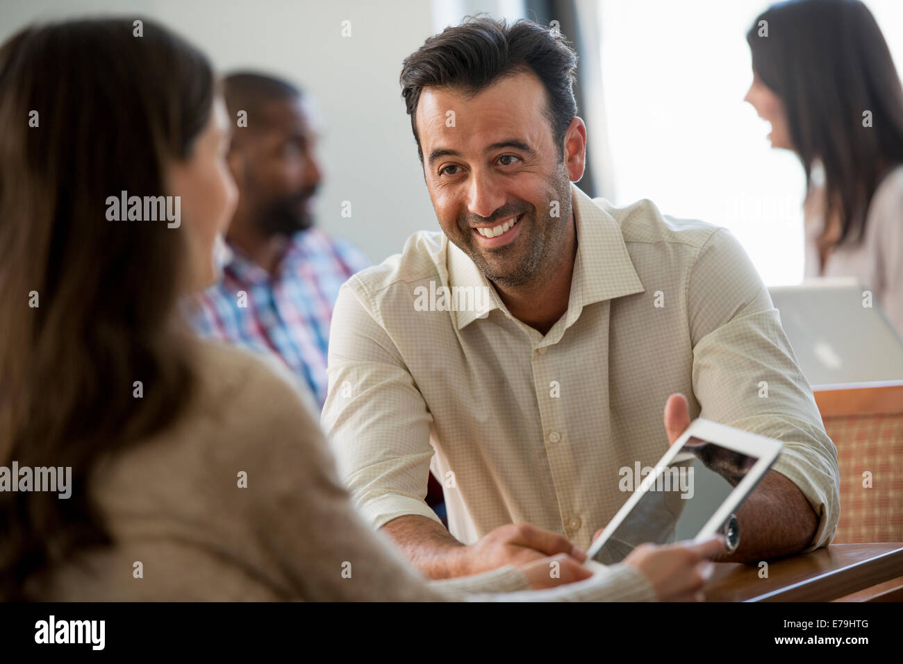 Quattro persone in un ufficio, due uomini e due donne. Due guardando una tavoletta digitale sullo schermo. Foto Stock