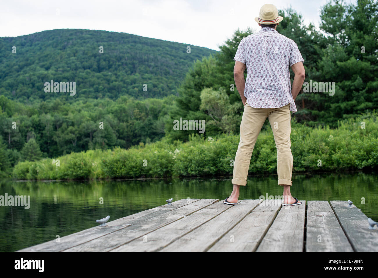 Un uomo in piedi su un molo in legno che si affaccia su di un lago calmo. Foto Stock