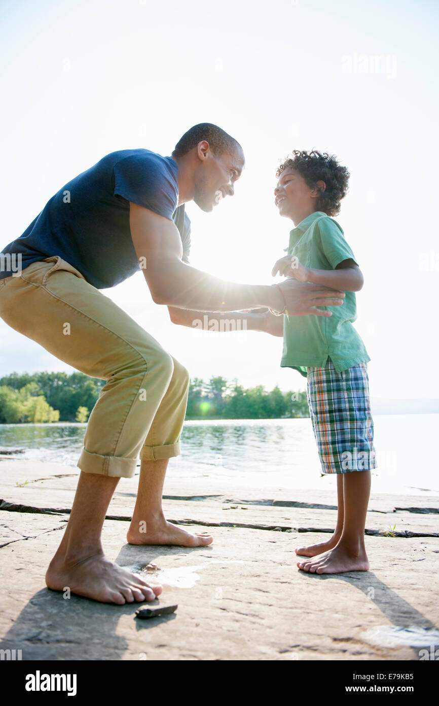 Un uomo di sollevare un piccolo ragazzo alto, giocando al sole in un lago. Foto Stock