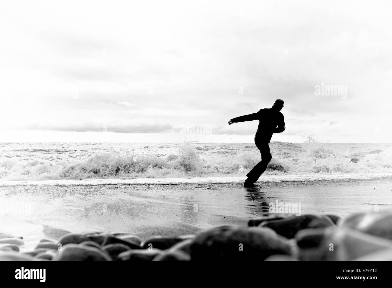 Silhouette di un giovane uomo che corre lungo la riva del mare Foto Stock